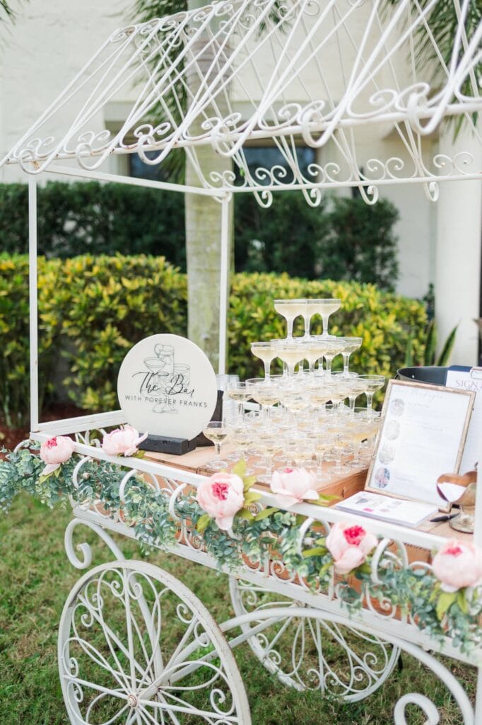 Champagne tower display on floral cart in the garden at Bonita Ranch wedding venue in Melbourne Florida