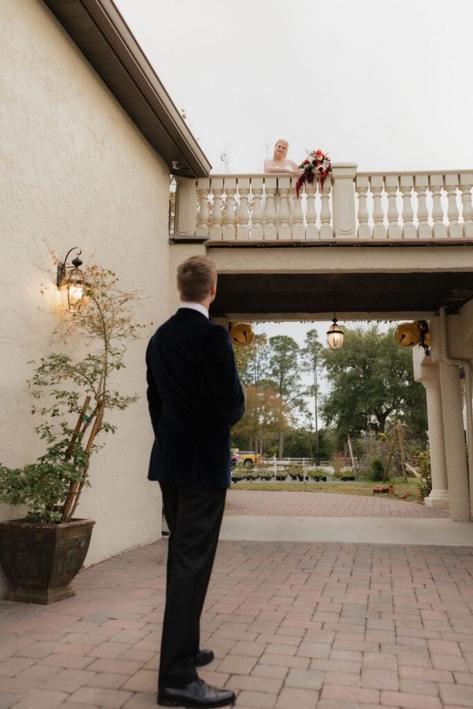 Bride on balcony looking down at groom during first look at Bonita Ranch destination wedding venue in Melbourne Florida