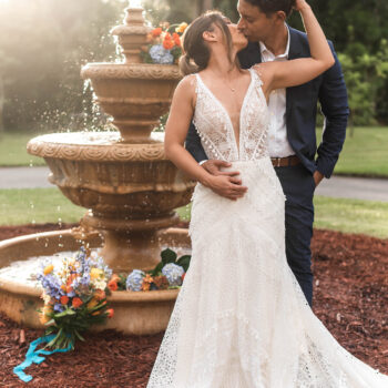 A couple posing by the stone fountain at Bonita Ranch during golden hour, with sunset in the background and colorful floral arrangements by Fern and Curl Florist, captured by Winship Photography.