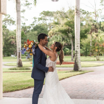 A couple posing under the Tuscan-style portico at Bonita Ranch, with the bride holding a vibrant, colorful bouquet in Melbourne, Florida.