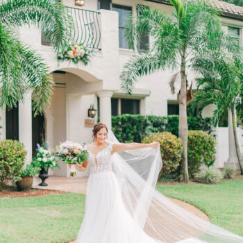 A bride playing with her flowing veil in front of the Mediterranean-style villa at Bonita Ranch wedding venue in Melbourne, Florida.